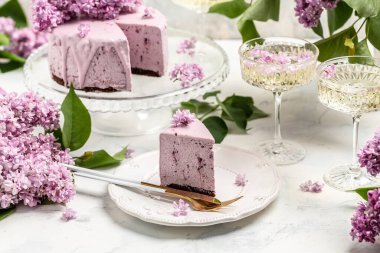 Bir parça kremalı pasta, taze böğürtlenli lezzetli tatlı yaban mersinli tart ve bir buket mor çiçek açan leylak.,