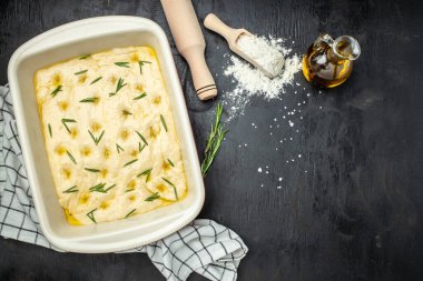 Pişirme kabında çiğ Focaccia hamuru. Siyah arka planda biberiyeli geleneksel İtalyan Focaccia 'sı. afiş, menü, metin için tarif yeri, üst görünüm.