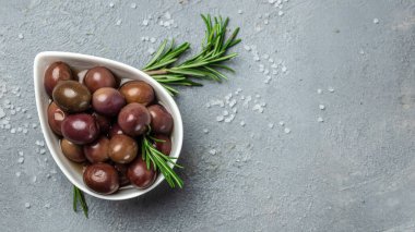 Gri arka planda küçük bir kasede taze biberiyeli kırmızı kalamar zeytinleri. Uzun afiş biçimi. en üstteki görünüm.