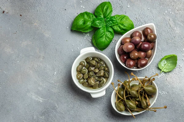 Various types of olives with fresh basil leaves on a gray background. Mediterranean snack assortment. banner, menu, recipe place for text, top view.