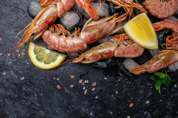 Red Argentine shrimps with ice and lemon, Wild shrimps, ocean jumbo shrimps on a dark background. Restaurant menu, dieting, cookbook recipe top view.