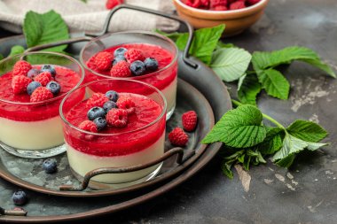 Ahudududulu panna cotta, üzerinde ahududu reçeli ve koyu bir arka plan. Küçük kavanozlarda krema soslu böğürtlen tatlısı. metin için yer.
