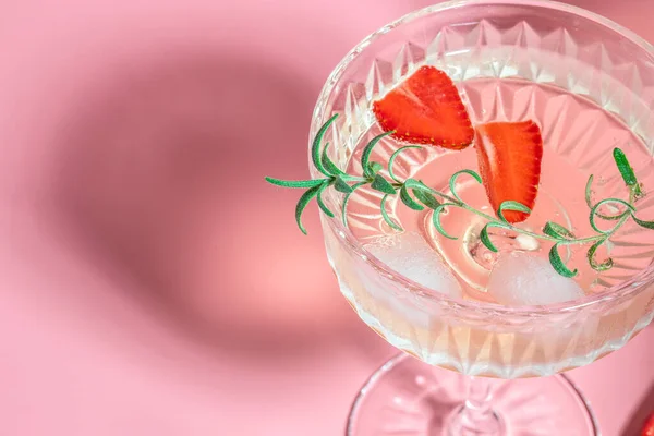 drink cocktail with ice in a glass on pink background. refreshing fruit cocktail or punch with wine champagne, strawberries, ice and rosemary.