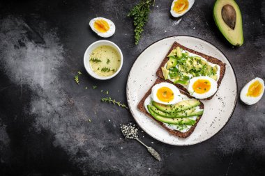 Avokado ile iki tost, haşlanmış yumurta ve koyu bir arka planda mikroyeşil. diyet ya da vejetaryen yemeği. dikey görüntü. Üst Manzara. metin için yer,