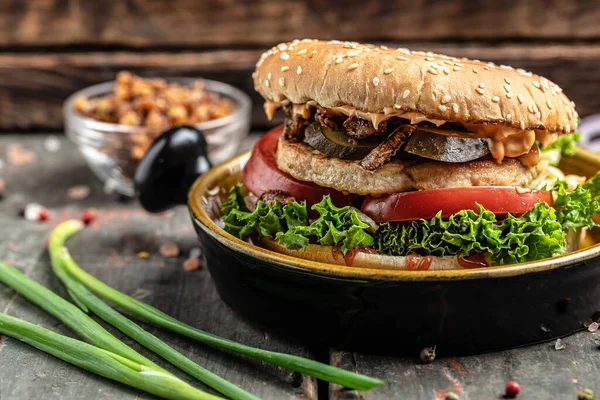 burger with grilled meat, vegetables, sauce on rustic wooden background. fast food and junk food concept,