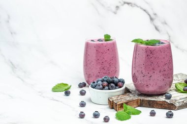 Böğürtlenli yoğurt, bardakta taze yaban mersini, nane yaprağı ve beyaz arka planda çiğ bira. Restoran menüsü, diyet, yemek kitabı tarifi üst görünümü.