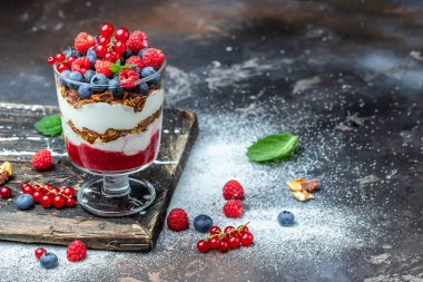 Yoğurtlu granola parfe yaban mersini ve ahududu ile koyu arkaplanda.