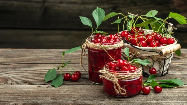 Jar of cherry jam and sour cherries. Berries cherry with syrup on a wooden background. Long banner format.