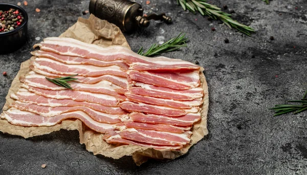 Close up Bacon slices. Pig meat. Pork belly with rosemary on a wooden board, Keto diet food ingredients. Restaurant menu, dieting, cookbook recipe.