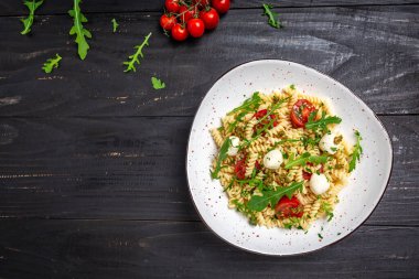 Domatesli Caprese salatalı makarna, koyu arkaplanda mozzarella sebze ezmesi, vejetaryen salatası, afiş, yazı için menü tarifi yeri, üst görünüm..