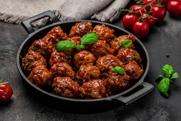 Meat or vegetable meatballs in tomato sauce in frying pan on dark background, top view.
