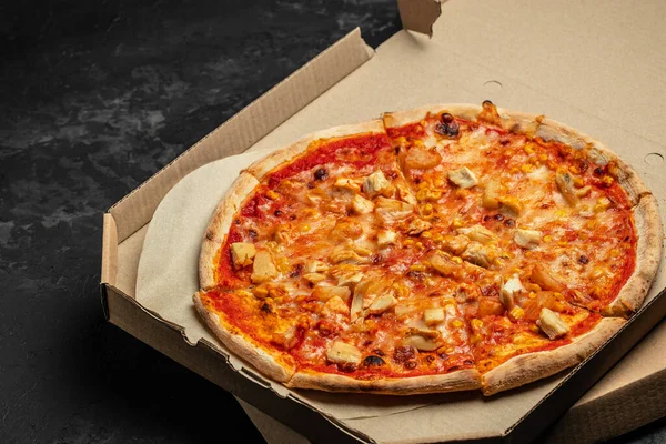 Tasty hawaiian pizza with chicken and pineapple on wooden cutting board in a paper box on a dark background. food delivery, place for text, top view,