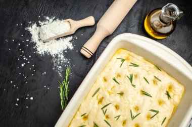 Pişirme kabında çiğ Focaccia hamuru. Siyah arka planda biberiyeli geleneksel İtalyan Focaccia 'sı. afiş, menü, metin için tarif yeri, üst görünüm.