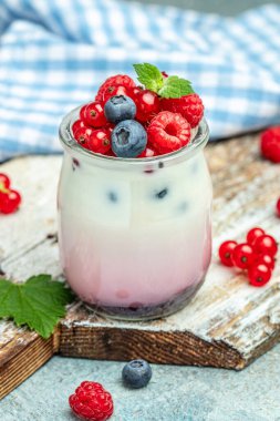 Ahududulu tatlı peynirli kek, ıvır zıvır, bardaktaki fare. Mavi arka planda ahududulu Yunan yoğurdu granola parfe. Restoran menüsü, diyet, yemek kitabı tarifi..