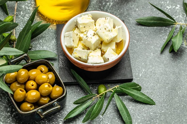 Feta cheese marinated in olive oil and young olives branch on dark background. top view. place for text.