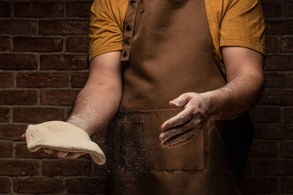 man kneading dough, baker with flour. Beautiful and strong men's hands knead the dough make bread, pasta or pizza. Powdery flour flying into air,