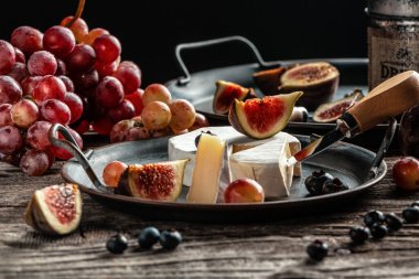Çeşitli peynir çeşitleri, geleneksel Fransız parçaları, İtalyan ve İspanyol manchego peyniri üzümlü ve incirli ahşap masada servis edilmiş..