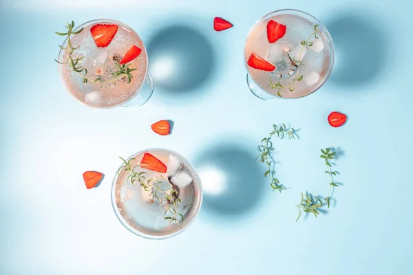 Glasses with cold pink champagne or punch with wine strawberries, ice and rosemary on blue background.