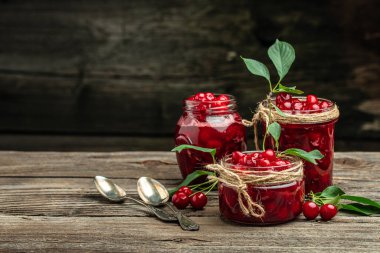 Fresh red cherries fruit on wooden background. Jar of cherry jam and sour cherries. Berries cherry with syrup. Canned fruit. place for text, top view.
