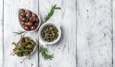 Gri arka planda taze fesleğen yapraklarıyla beyaz tabakta kapari üzümü ve zeytin. Akdeniz atıştırmalıkları. afiş, menü, metin için tarif yeri, üst görünüm.