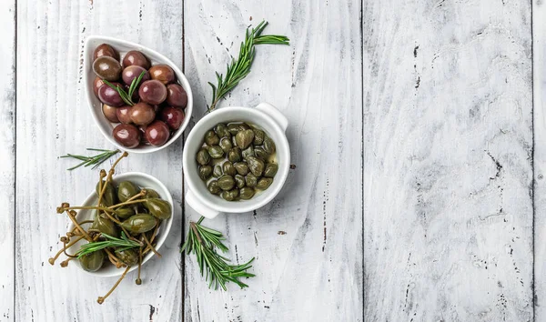 Gri arka planda taze fesleğen yapraklarıyla beyaz tabakta kapari üzümü ve zeytin. Akdeniz atıştırmalıkları. afiş, menü, metin için tarif yeri, üst görünüm.