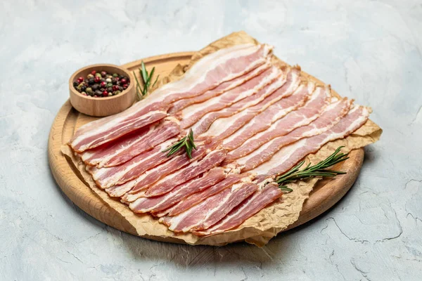 Close up Bacon slices. Pig meat. Pork belly with rosemary on a wooden board, Keto diet food ingredients. Restaurant menu, dieting, cookbook recipe.