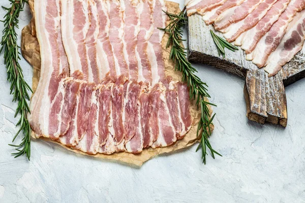 Close up Bacon slices. Pig meat. Pork belly with rosemary on a wooden board, Keto diet food ingredients. Restaurant menu, dieting, cookbook recipe.