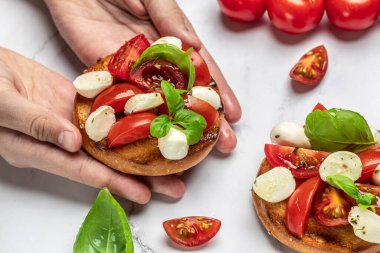 Mutfakta Caprese Bruschetta 'yı tutan kadın eller. Lezzetli kahvaltı ya da atıştırmalık, temiz yemek, diyet, vejetaryen yemek konsepti. en üstteki görünüm.