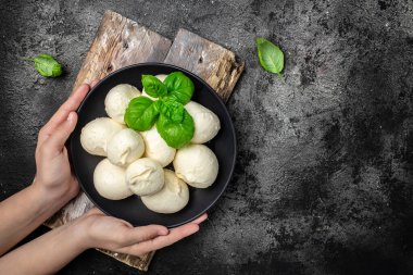 Beyaz İtalyan peynirli mozzarella topları tutan kadın eller, kırmızı vişneli domates ve taze fesleğen yapraklarıyla servis ediliyor. metin için yer, üst görünüm.