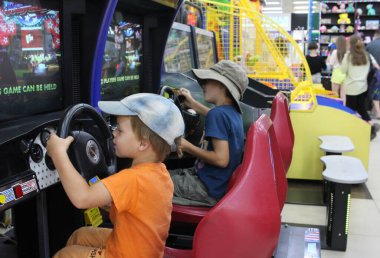 Rusya, Novosibirsk 20.07.2021: Alışveriş ve eğlence merkezindeki çocuk kardeşler direksiyonda oyuncak arabalarla oynuyorlar