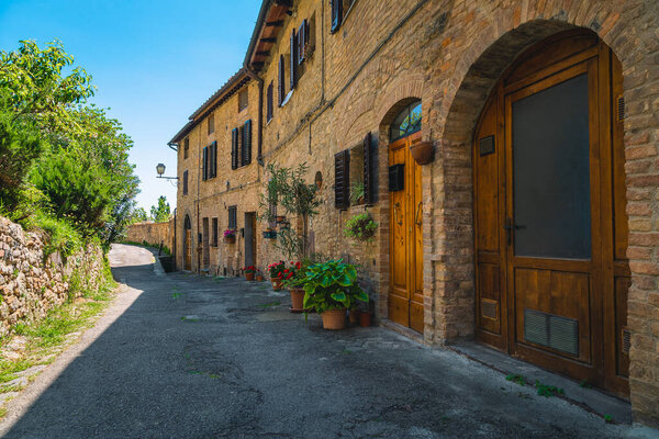 Rustic tuscan brick houses and cozy entrances decorated with colorful flowers. Fantastic street view in San Gimignano, Tuscany, Italy, Europe