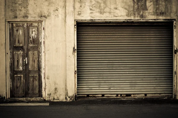 Porta do obturador de rolo metálico grunge iluminado perto da porta de madeira — Fotografia de Stock