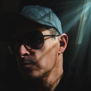 Şapkalı ve güneş gözlüklü bir adam gölgelerde selfie çekiyor. 