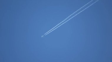 Gökyüzünde yükseklerde uçan jet uçağı açık mavi gökyüzünde kontrastlar bırakır..