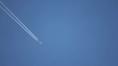 Gökyüzünde yükseklerde uçan jet uçağı açık mavi gökyüzünde kontrastlar bırakır.