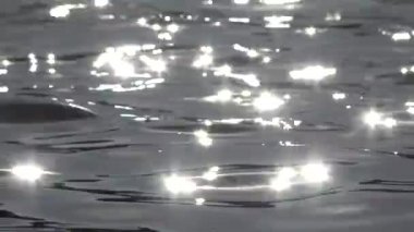 Parlak güneş ışığını çok yumuşak bir bokeh ile yansıtan bir gölde dalgalı suyun seçici odağı.