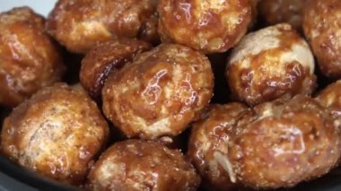 Beyaz arka plana karşı küçük bir kasede dönen bir sürü şekerli macadamia fındığı..