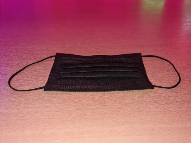 Siyah tıbbi korona maskesi pembe arka planda izole edilmiş.