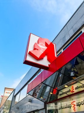 Alışveriş merkezindeki Aesculap eczanesinin girişi ve kırmızı logosu.