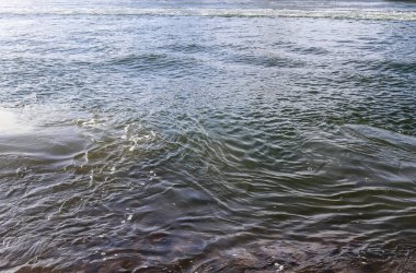 Dalgalar ve dalgalarla su yüzeyi ve güneşli bir günde ışığı yansıtan güneş ışığı.