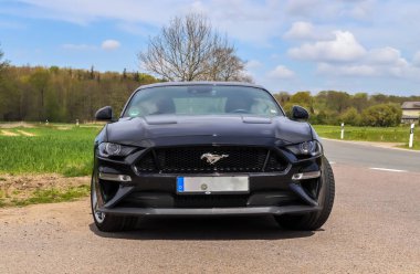 Kiel, Almanya - 30.April 2022: Kumlu bir yolda park edilmiş siyah bir Ford Mustang 2018 model spor araba üzerinde ön görüş