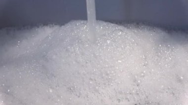 Foam and soap bubbles from water in a sink with water running from a water tap