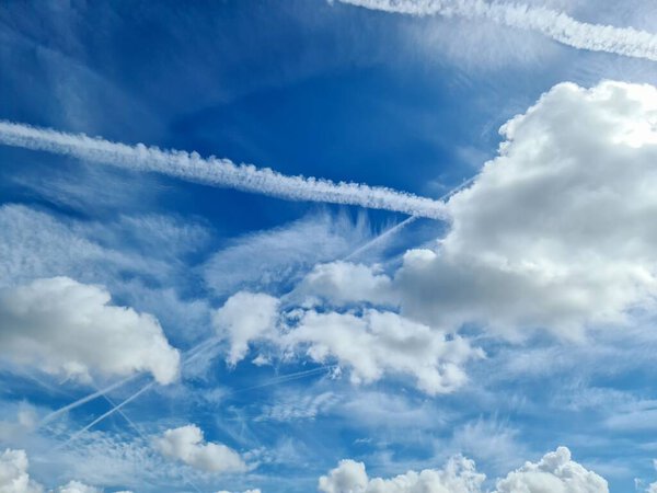 Aircraft condensation contrails in the blue sky inbetween some beautiful clouds