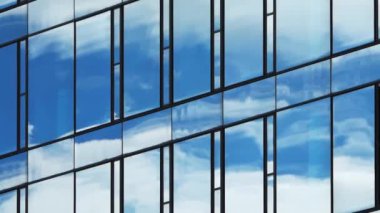 Bir ofis binasının cam cephesinden yansıyan bulutlarla dolu mavi bir gökyüzünün zaman akışı..