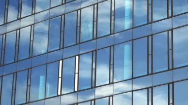 Bir ofis binasının cam cephesinden yansıyan bulutlarla dolu mavi bir gökyüzünün zaman akışı..