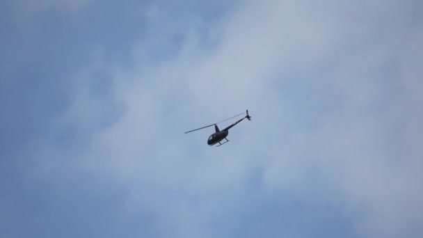 一架黑色的小直升机在蓝天和多云的天空中呈弧形飞行 — 图库视频影像