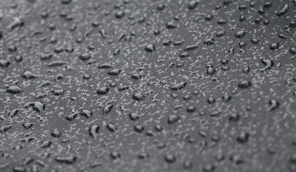 Rain drops on a black metallic surface in a closeup view