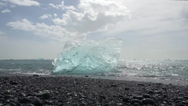青い氷山が黒い砂の上で溶けているアイスランドのダイヤモンドビーチと太陽の光で輝く氷 — ストック動画