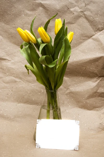 Tulipas amarelas em um vaso e um cartão branco — Fotografia de Stock