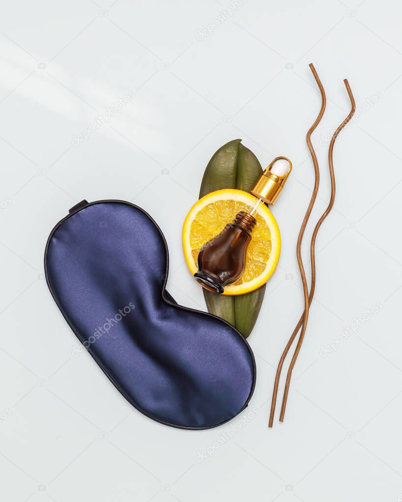 Spa relax composition with sleep mask, orange slace and orange oil in a jar on a blue background. Orange oil is the best natural remedy for the treatment of depression, insomnia and nervous stress